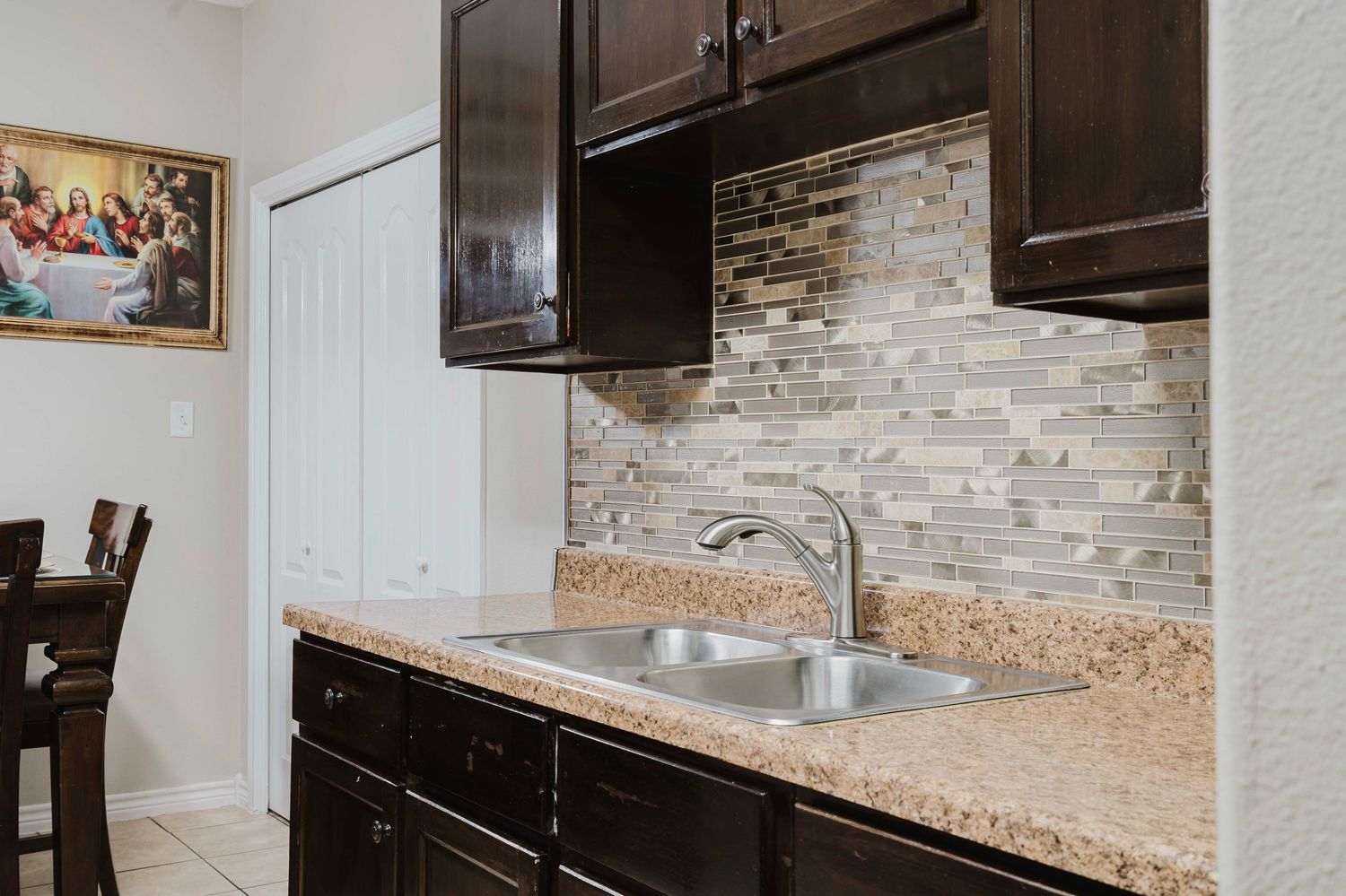 Modern kitchen features dark wood cabinets, granite countertops and a stone tile backsplash with stainless steel sink.