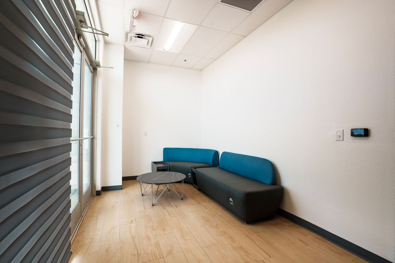 Modern office waiting area with blue cushioned bench seating, hardwood floors, and steel rolling door in a minimalist space.
