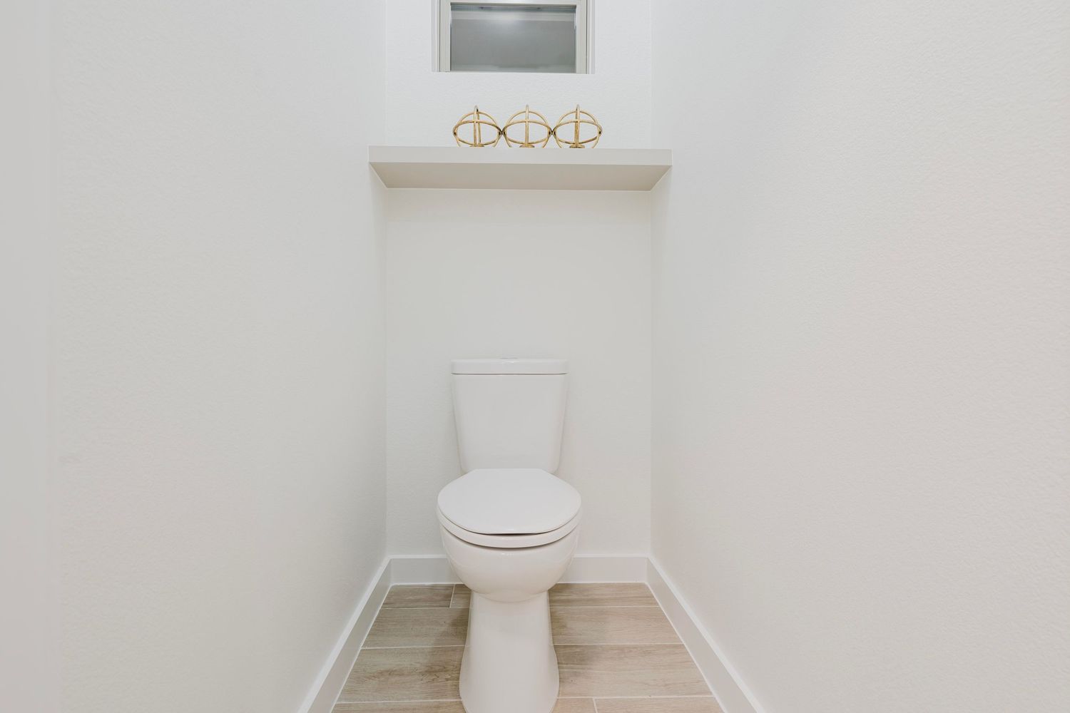 Minimalist powder room featuring white toilet, gold light fixtures, and light wood floors.