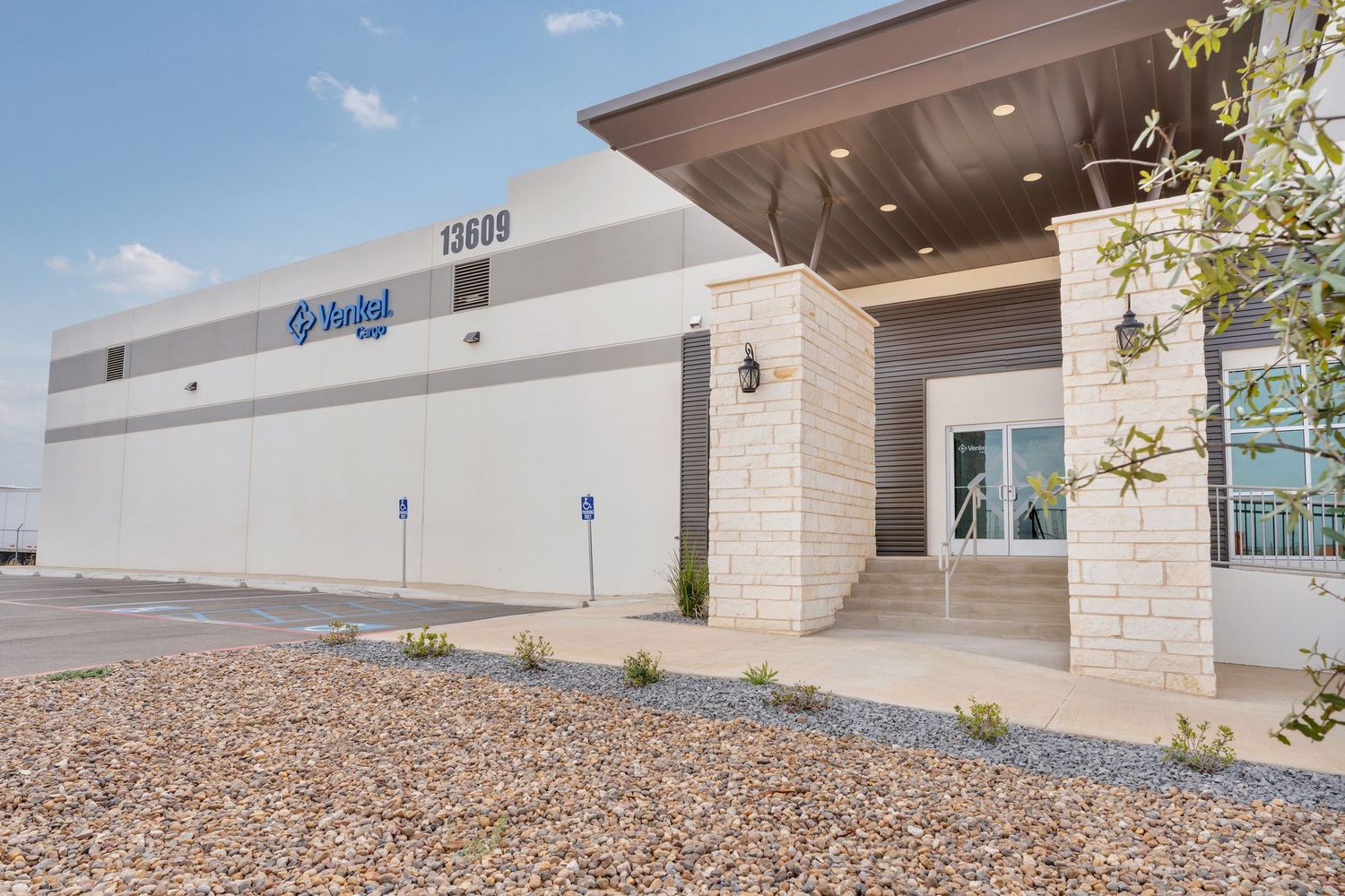Modern commercial building exterior with desert landscaping and rock ground cover under bright blue sky.