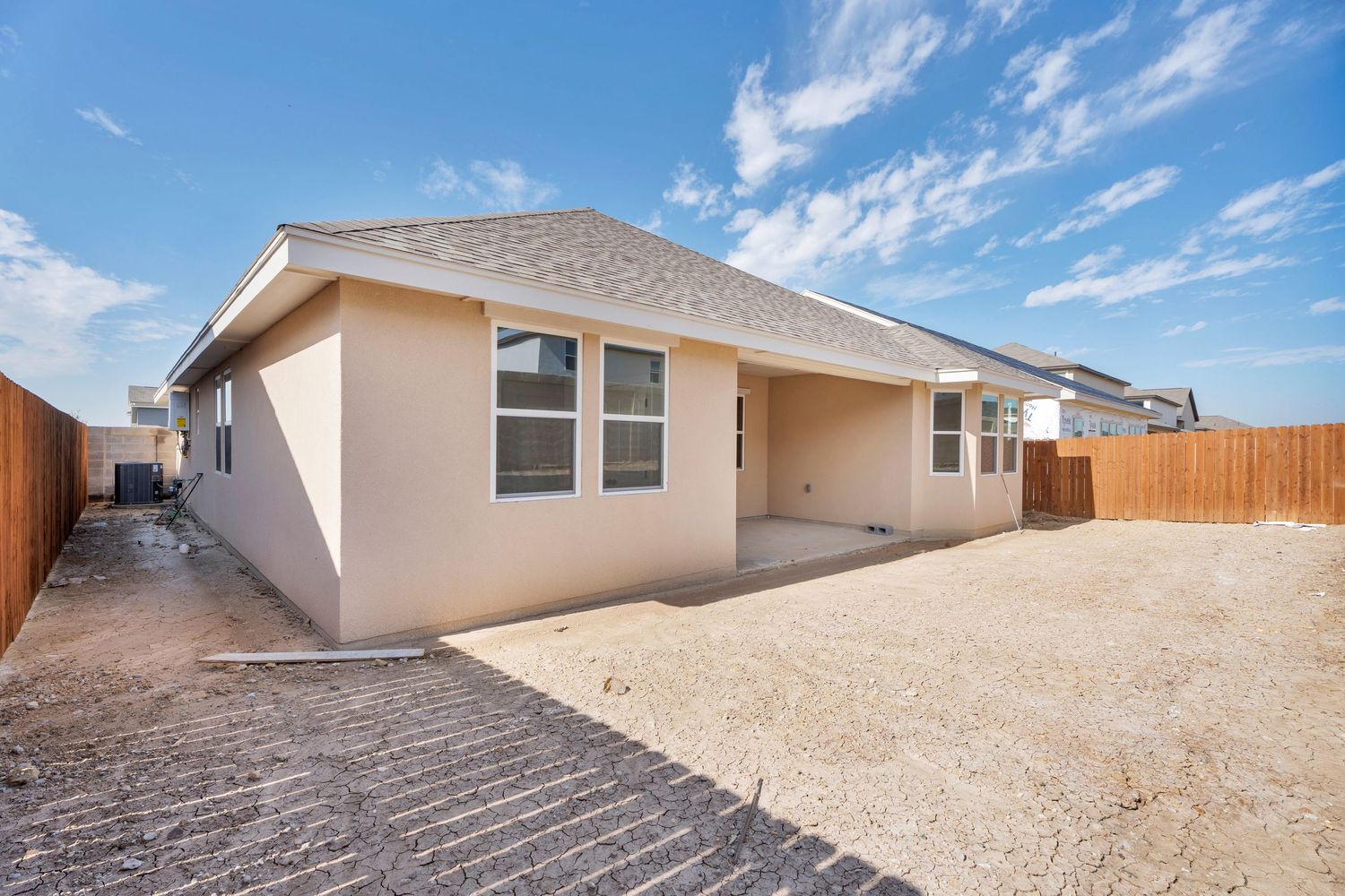 Desert landscaping with rock ground cover surrounds a modern beige stucco home under bright blue skies.