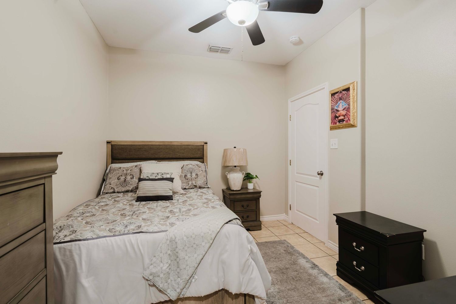 Cozy bedroom with black furniture, a ceiling fan, and patterned bedding in neutral tones.