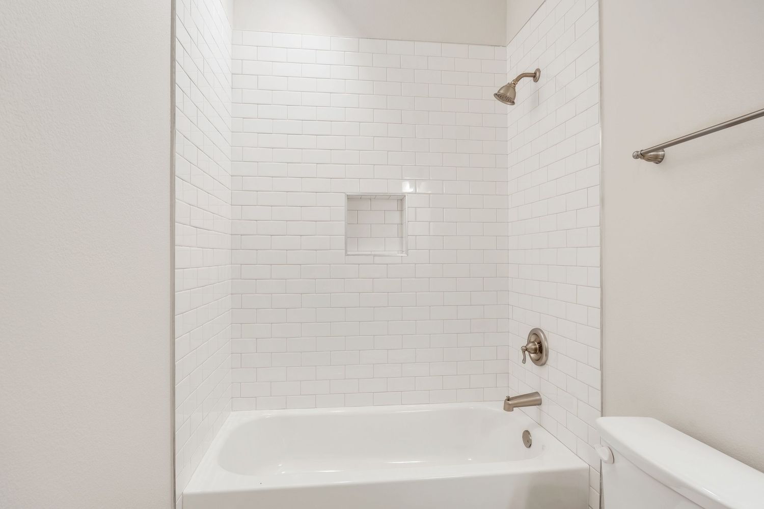 Modern white bathroom interior with subway tile walls, recessed shelving niche, and bronze shower fixtures.