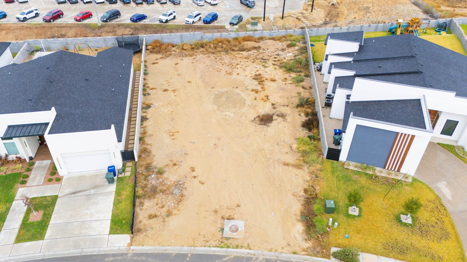 Aerial view of a residential construction site showing foundation work and surrounding houses in a developing neighborhood.