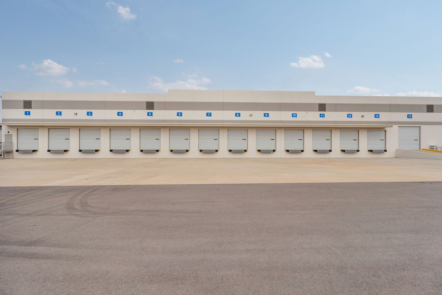 Loading dock doors line the exterior of a beige commercial warehouse building with tire marks on the concrete pavement.