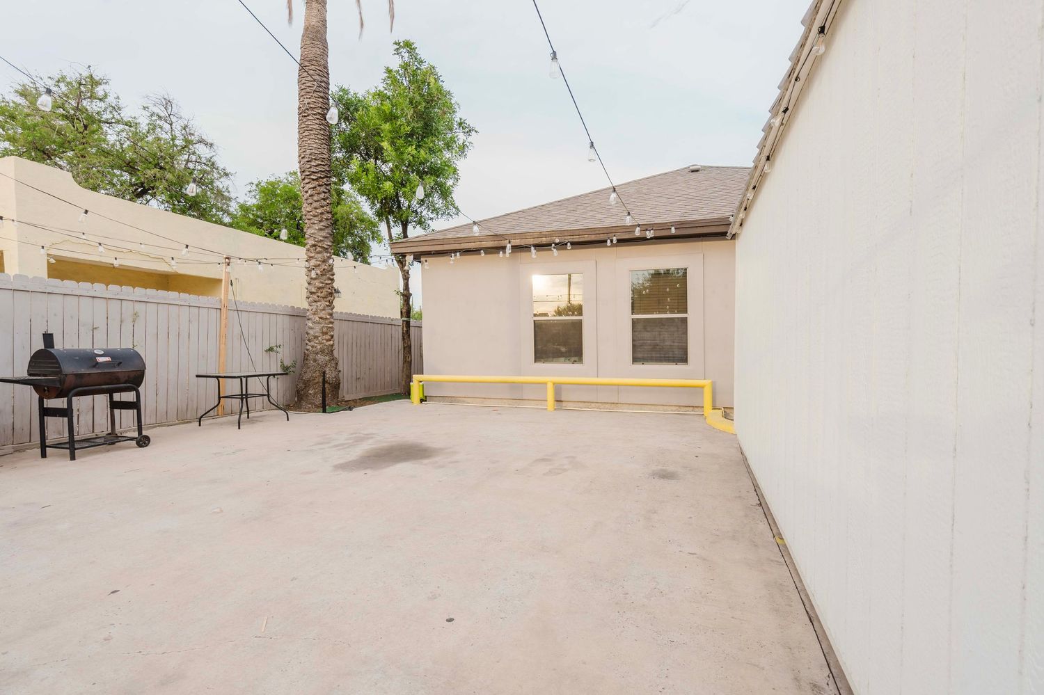Spacious concrete patio with BBQ grill and privacy fence enclosed by white walls and palm trees.