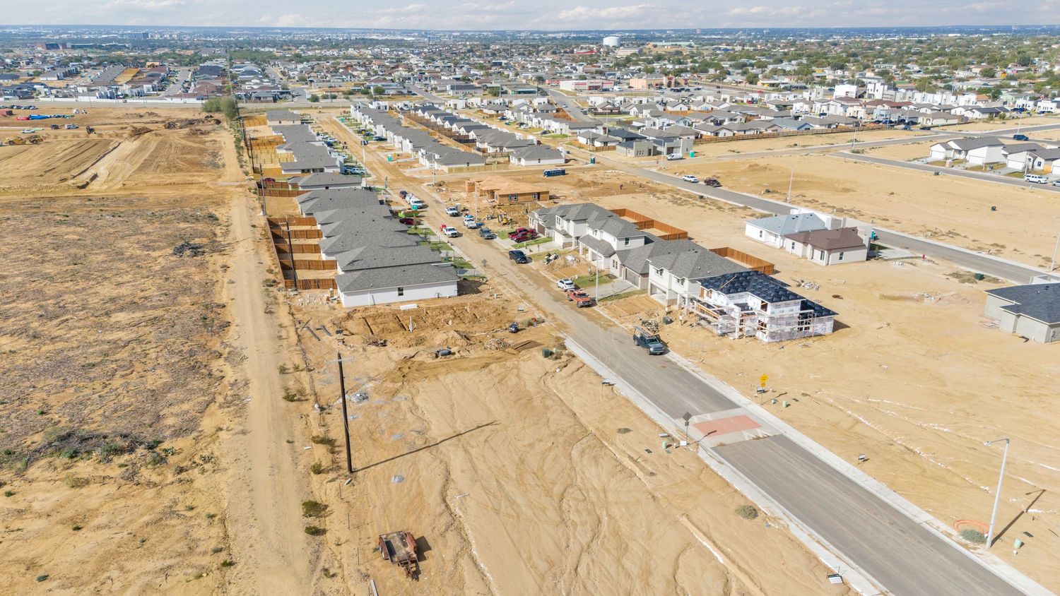 Aerial panoramic view of residential development and construction sites in a desert landscape with new roads and infrastructure.