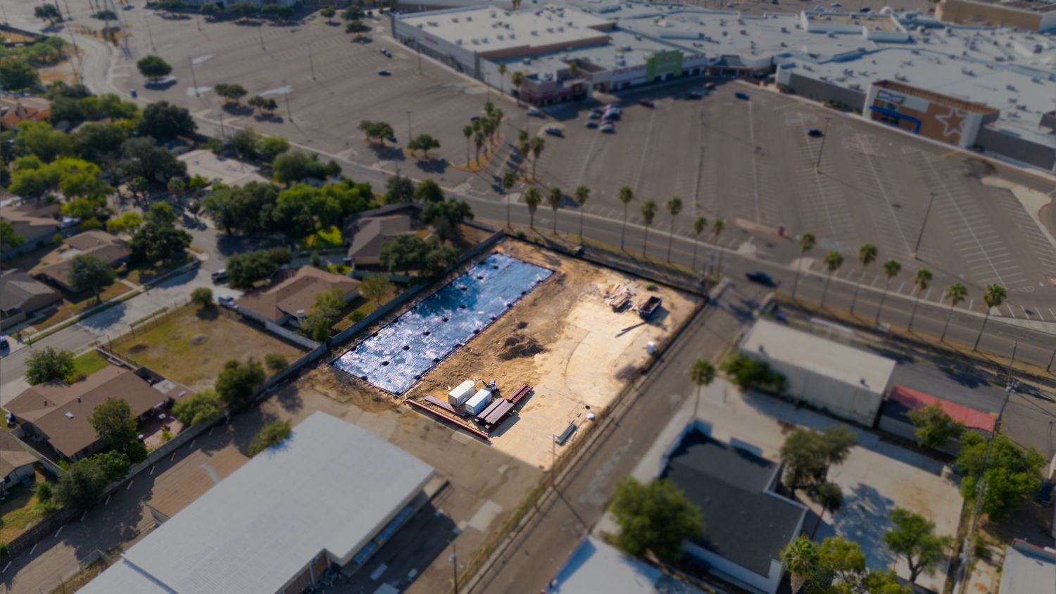 Wide aerial view of an industrial complex with warehouses, parking lots, and shipping containers under a blue sky.