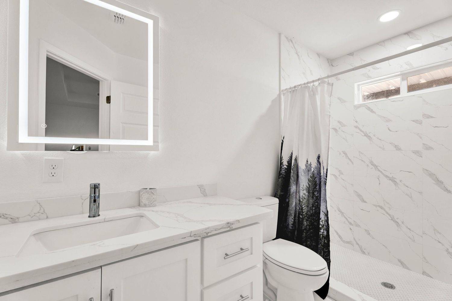 Bright white bathroom with double vanity, marble countertop, LED mirror, and forest shower curtain.