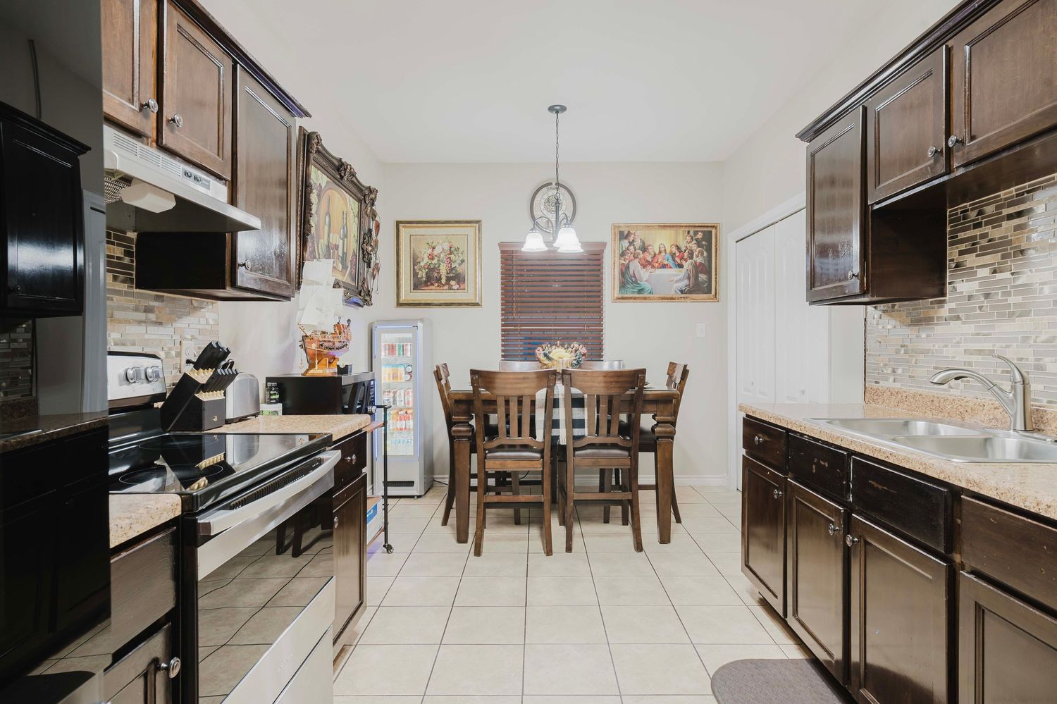 Modern galley kitchen with dark wood cabinets, black appliances, stone backsplash and dining area with pendant light.