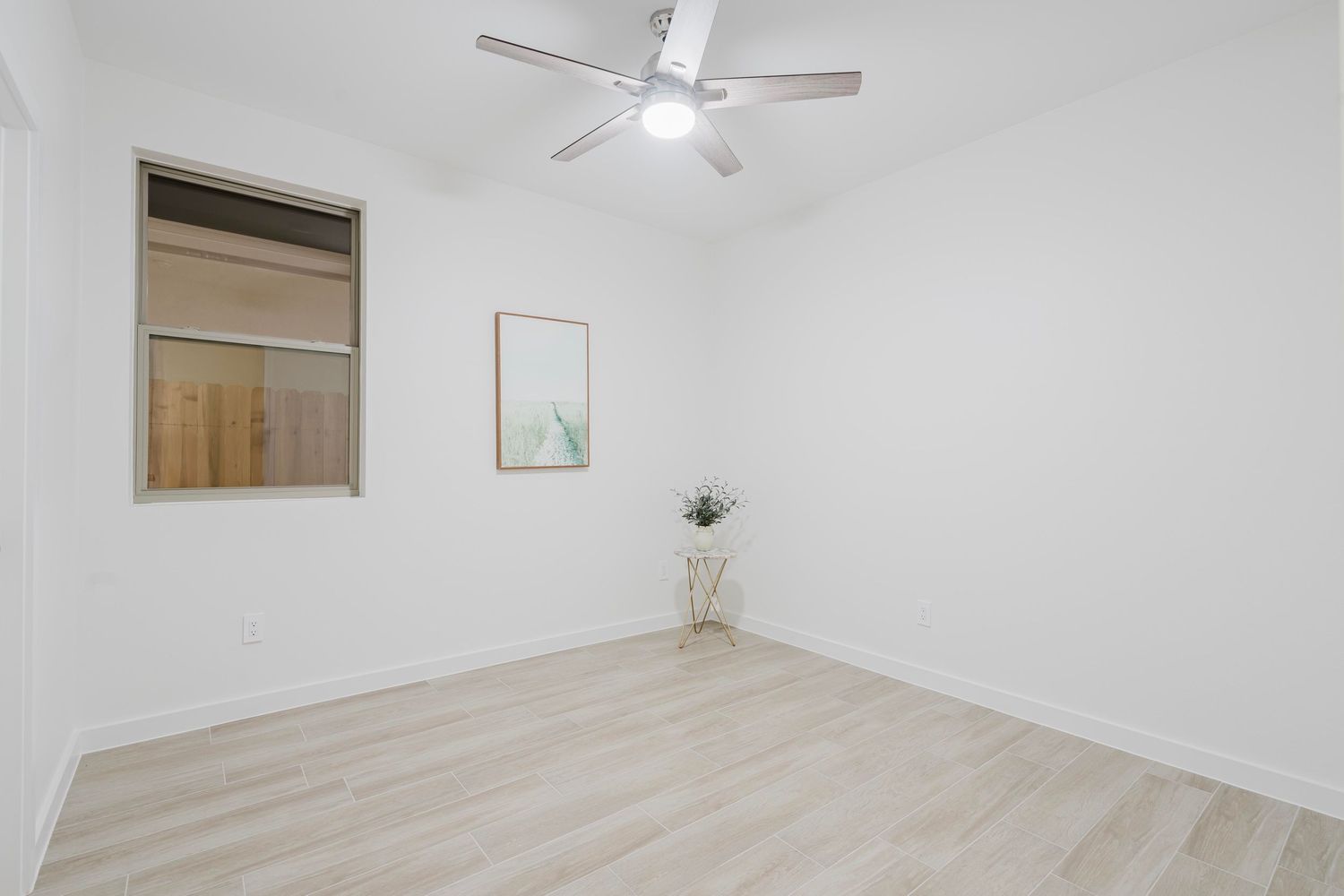 Minimalist bedroom with light wood flooring, ceiling fan, and small window.