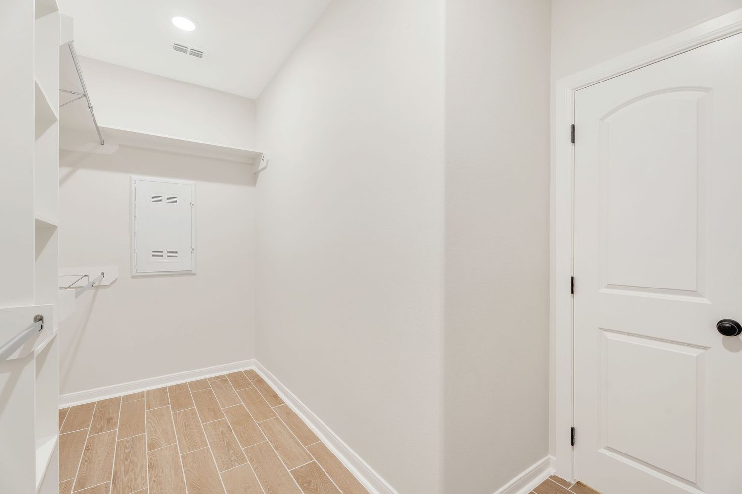 Empty laundry room with white walls, wooden floor tiles, and a white door features built-in shelving and utility hookups.
