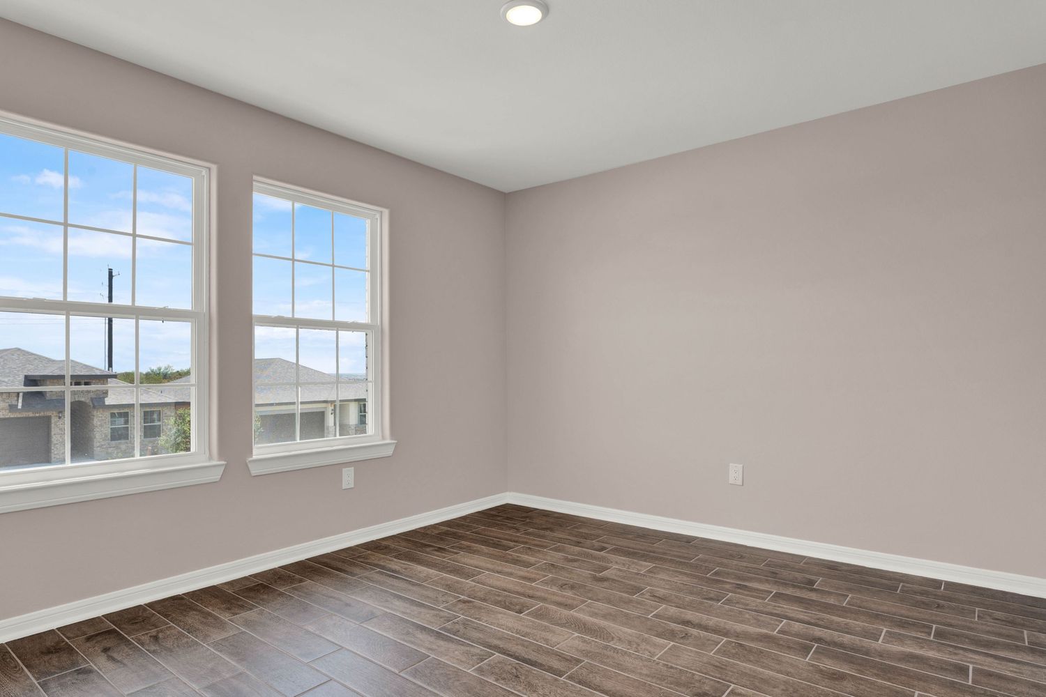 Empty room with dark hardwood floors, light gray walls, white baseboards, and two large windows with natural light.