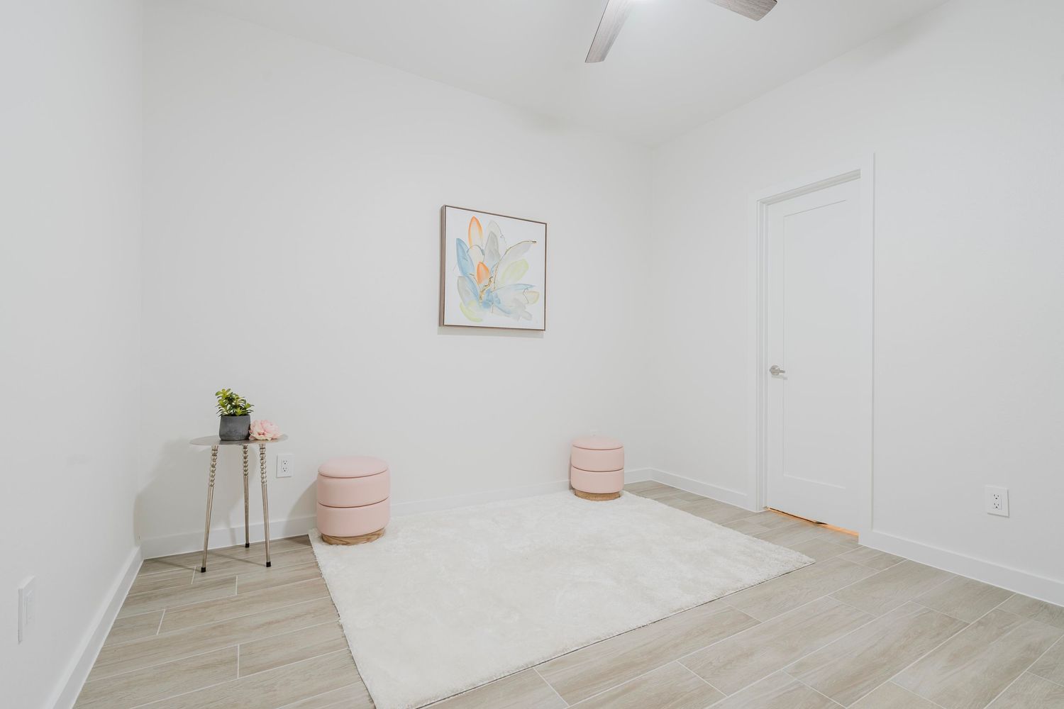 Bright room with light wood flooring, pink poufs, and minimal wall art.