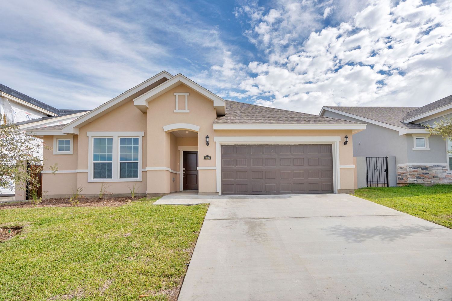 A series of identical suburban homes with beige exteriors and concrete driveways under a cloudy sky.