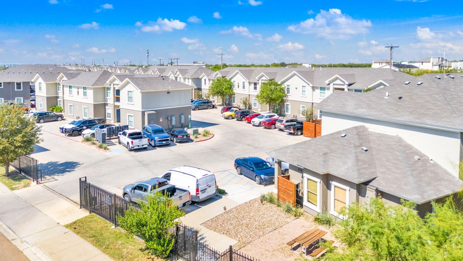 Panoramic aerial view of a residential neighborhood with townhomes and parking lots under bright blue skies.