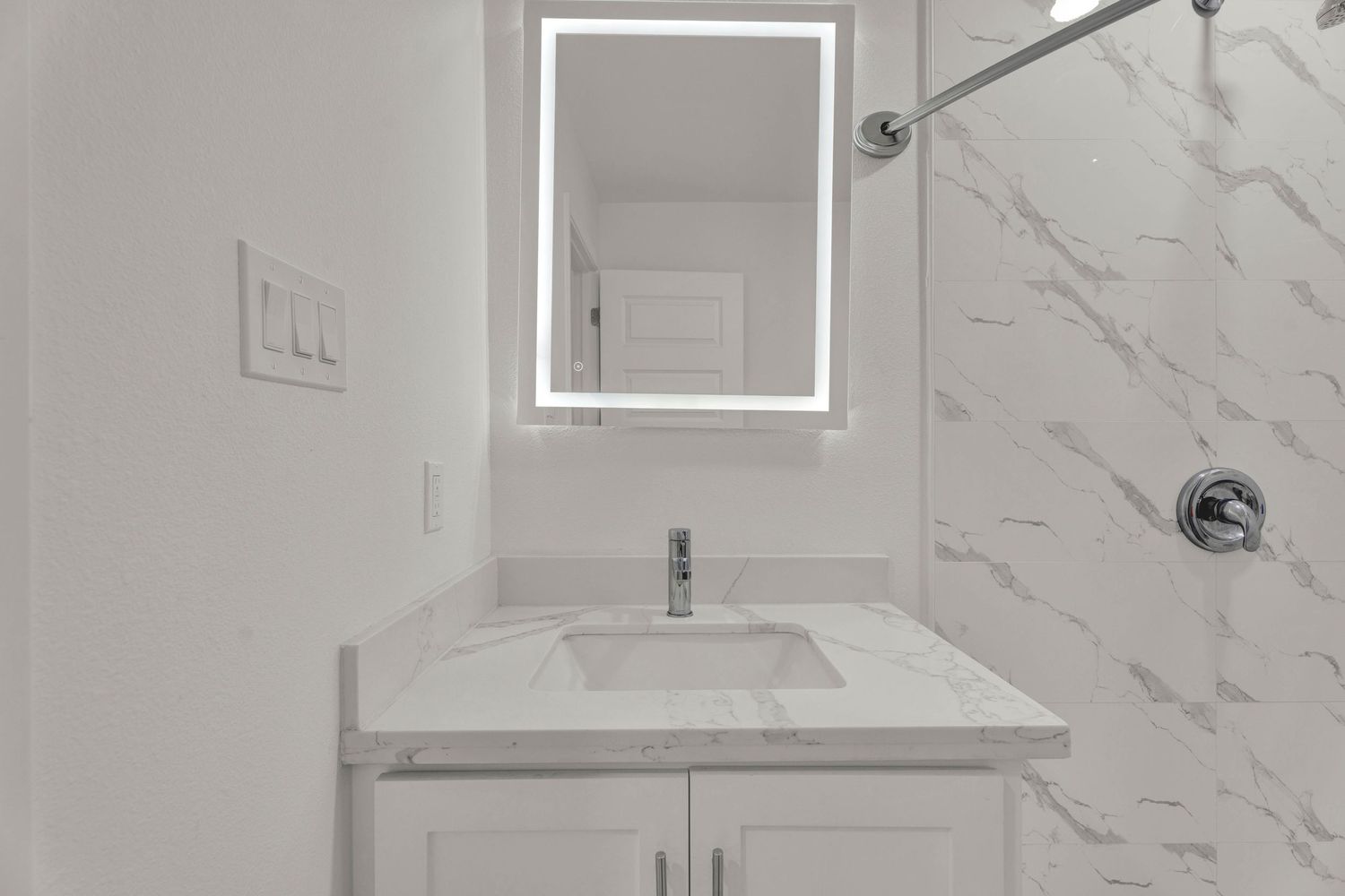 Modern bathroom vanity with marble countertop, undermount sink, LED mirror, and white cabinets.