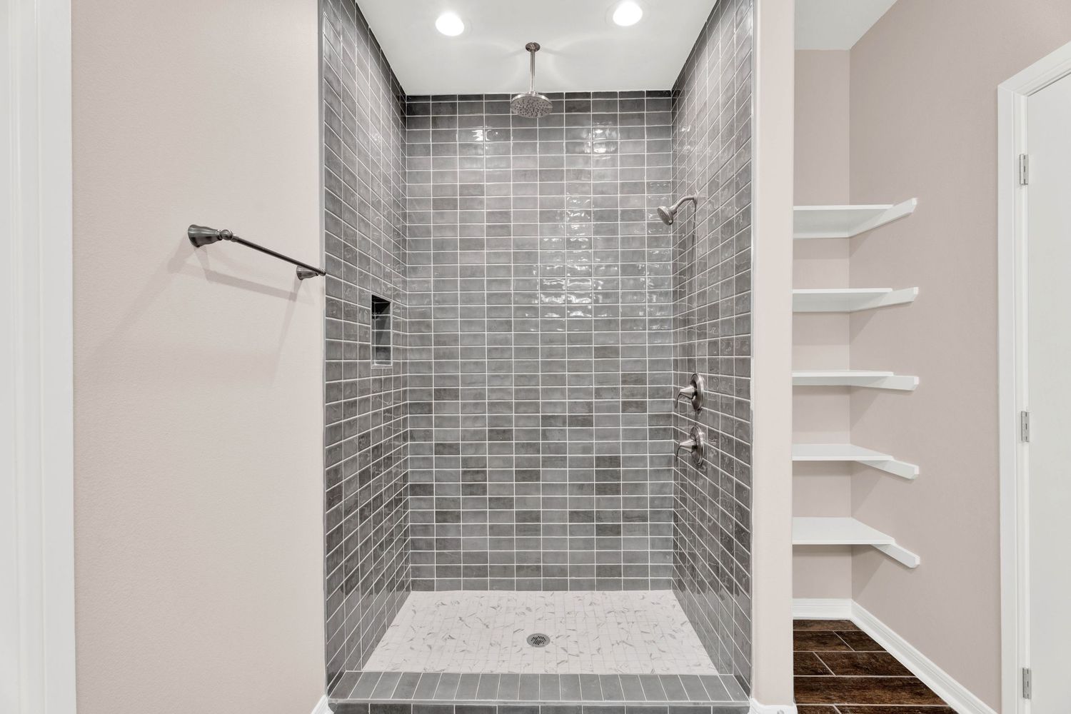Walk-in shower with gray subway tile walls, mosaic tile floor, built-in shelving, and a rainfall showerhead.