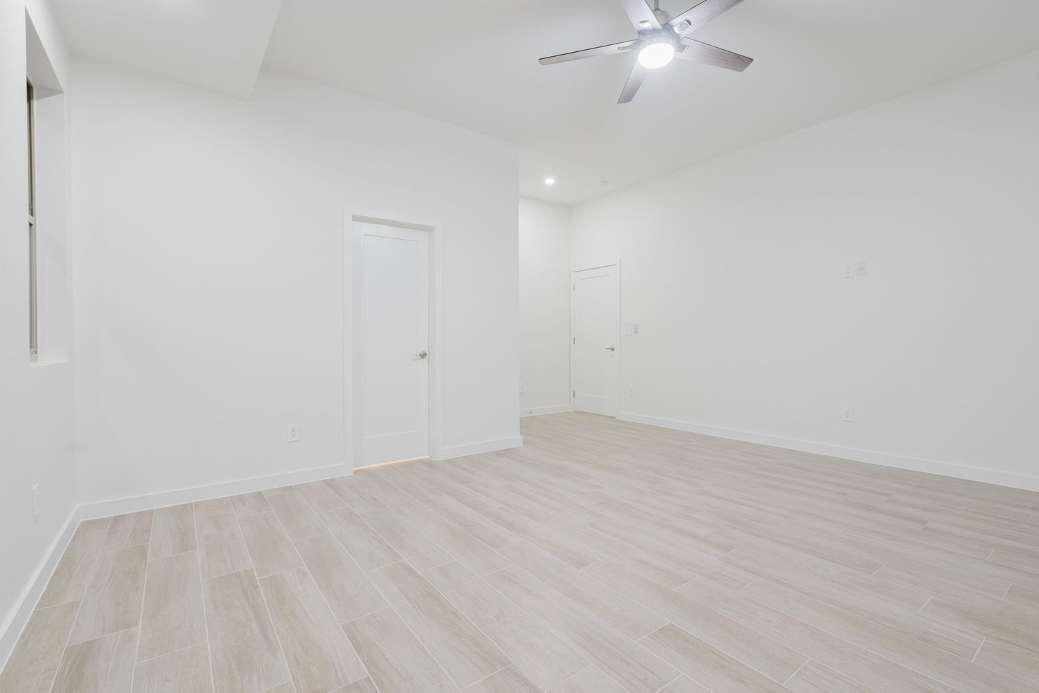 Empty white room with light wood flooring and ceiling fan.