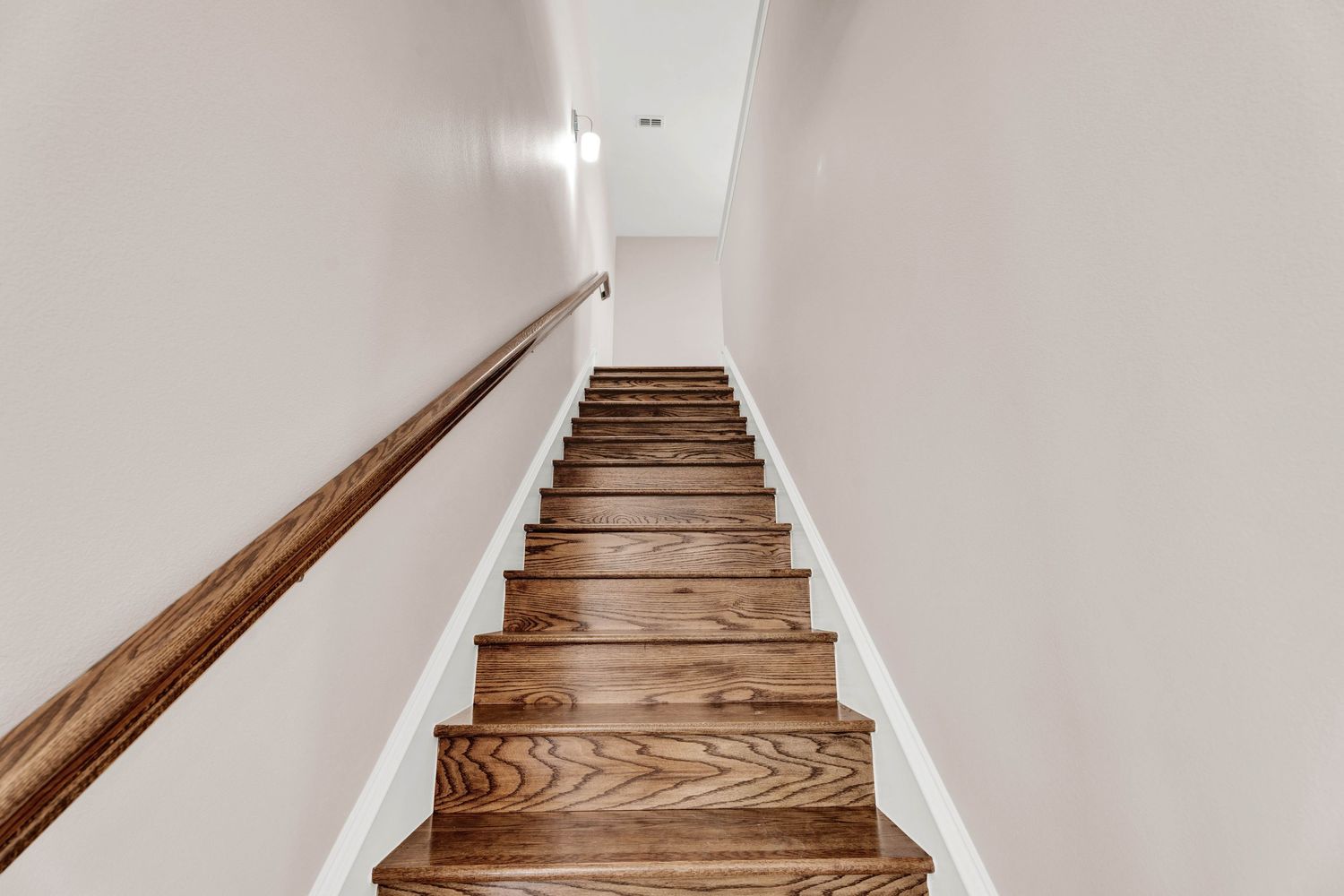 Narrow staircase with rich hardwood steps, white risers, and a wooden handrail leading upstairs.