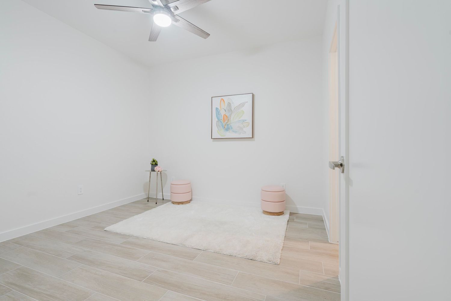 Minimalist white room with light wood floors, ceiling fan, and pink decor accents.