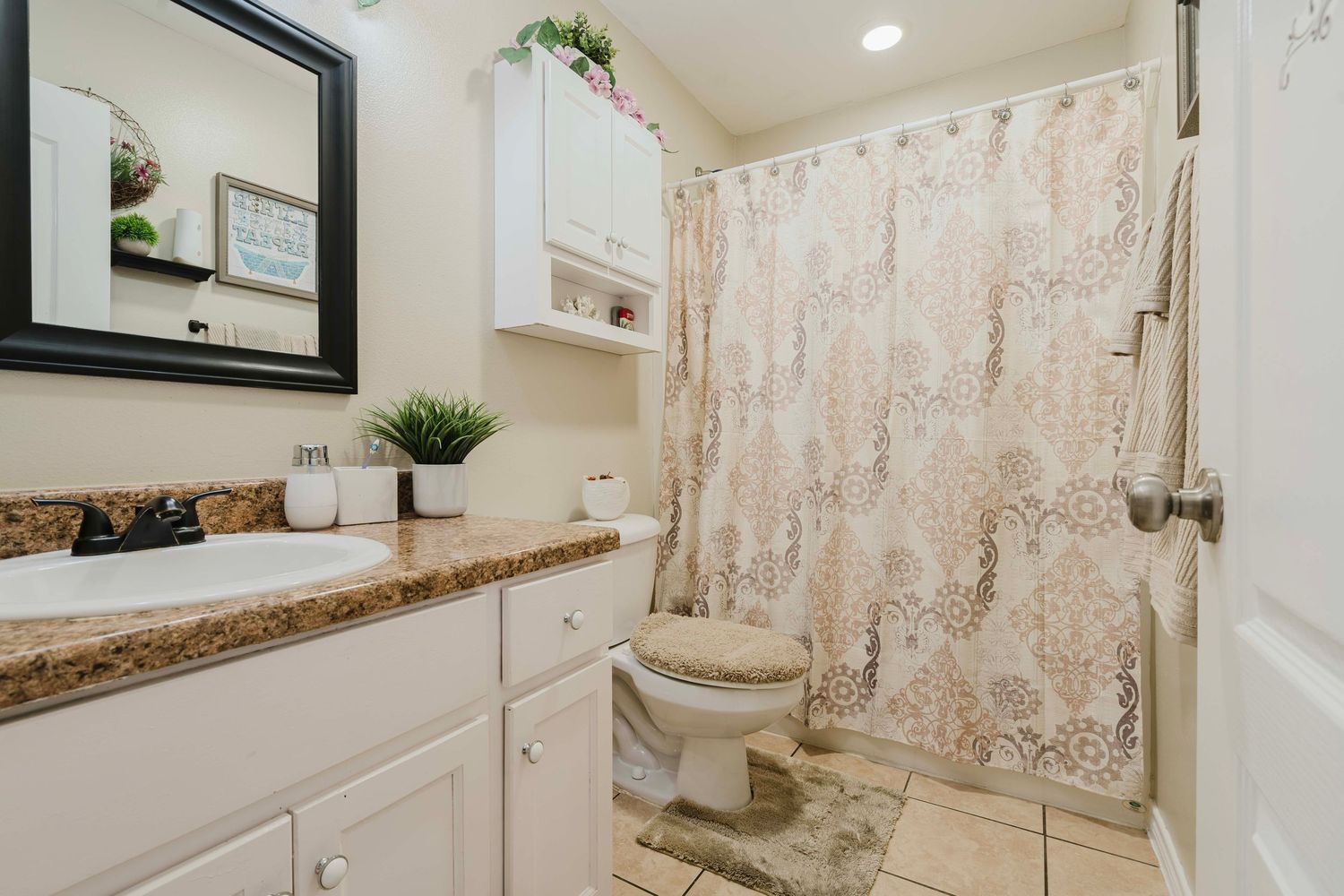 Modern bathroom with granite countertop, white cabinets, and floral shower curtain features clean minimalist design.