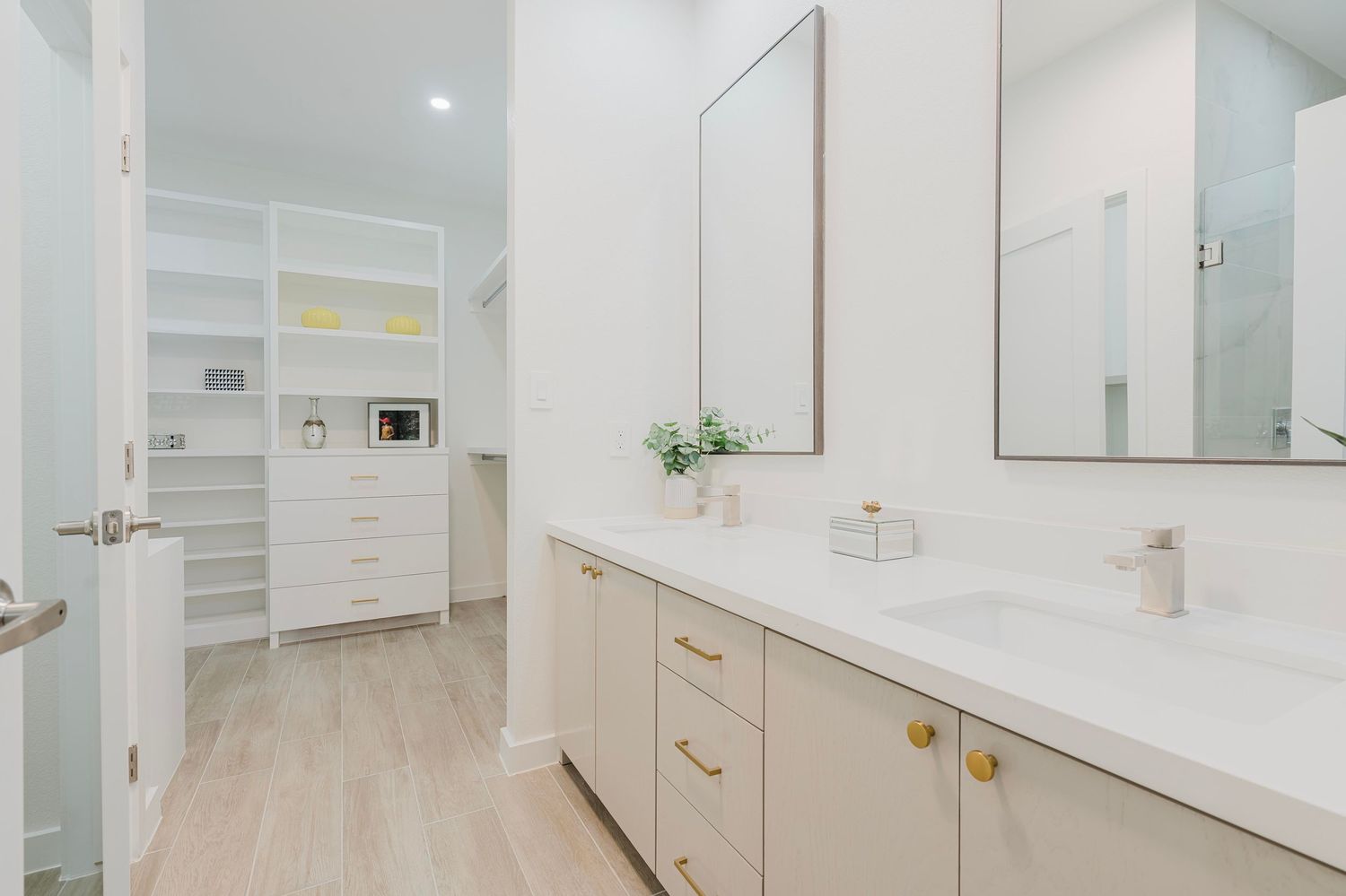 Bright bathroom interior featuring white cabinets, light wood flooring, and gold accent handles.