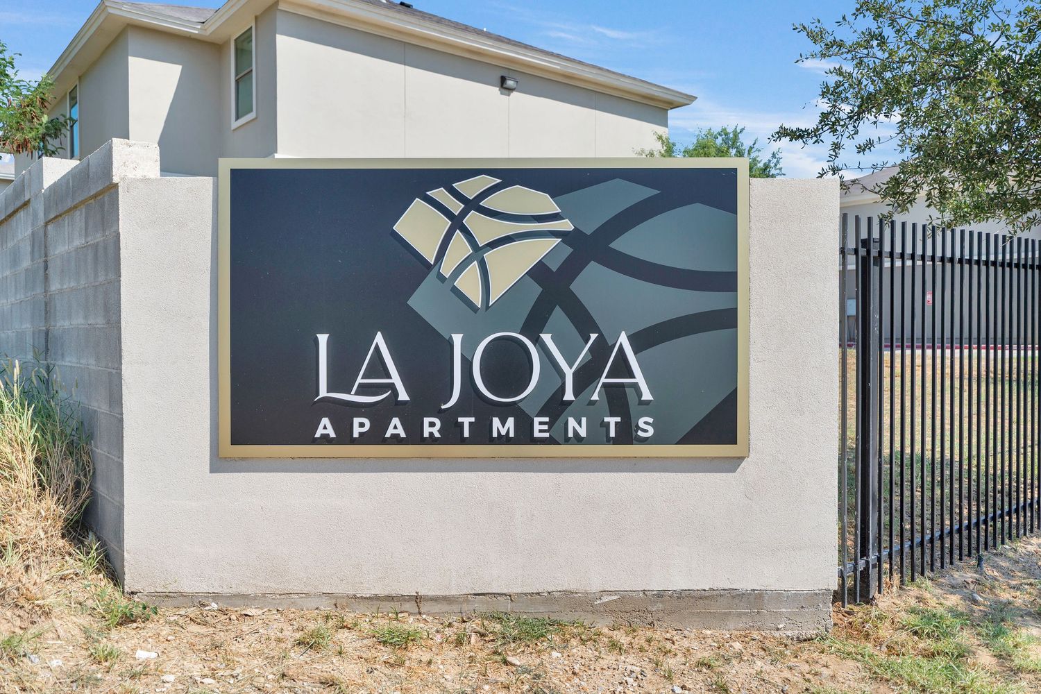 Modern apartment complex entrance with white walls, iron gates, and La Joya signage in an upscale setting.