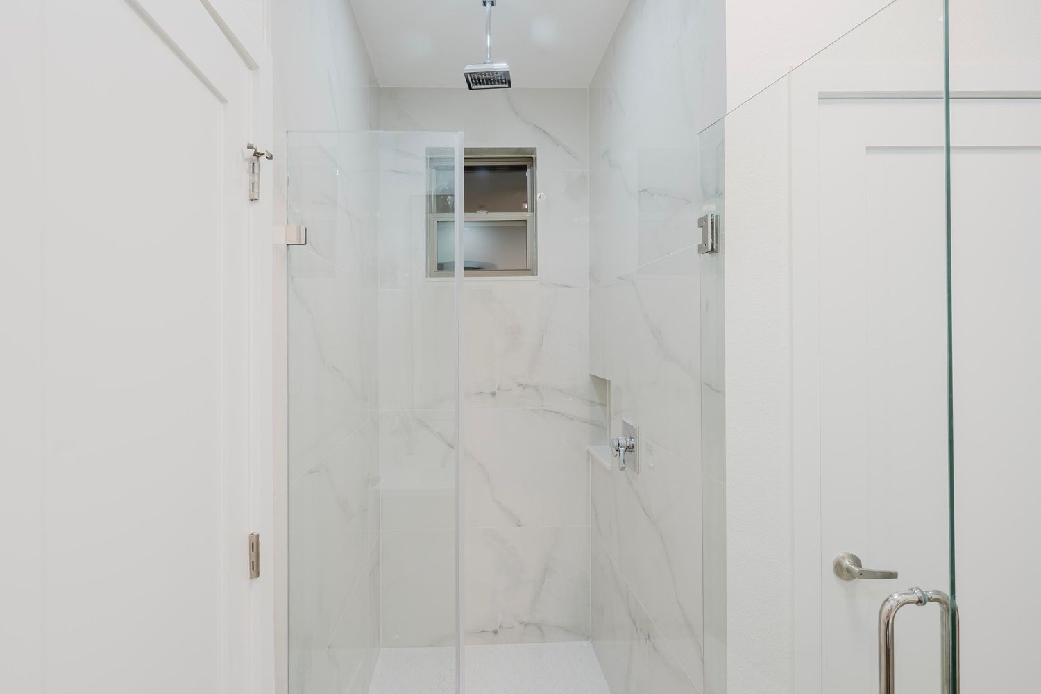 Minimalist white marble shower enclosure with glass door and chrome fixtures.
