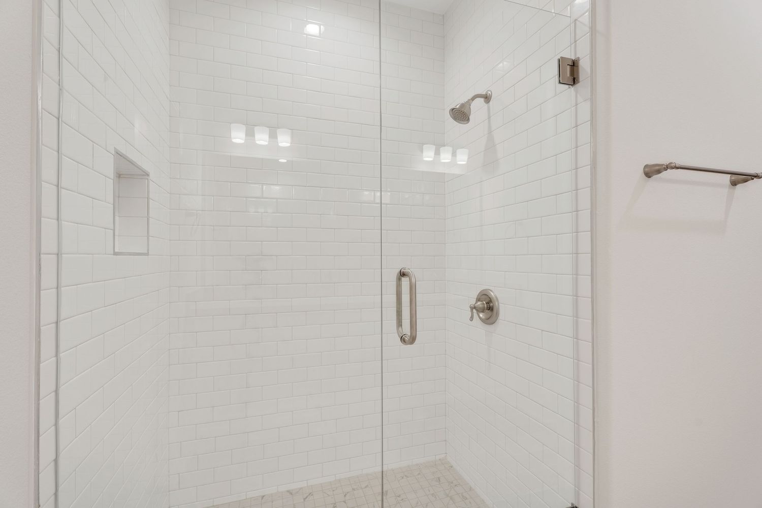 Modern bathroom interior with white subway tile walls, glass shower enclosure, and chrome fixtures.