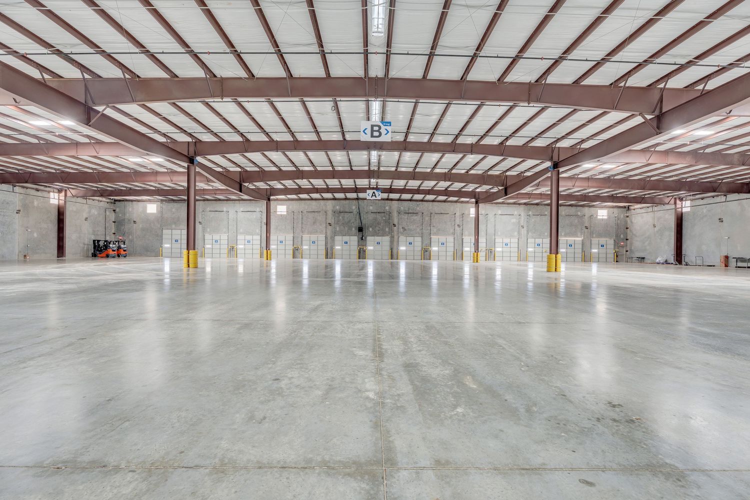 Large empty industrial warehouse interior with concrete floors and metal ceiling beams shows construction progress.