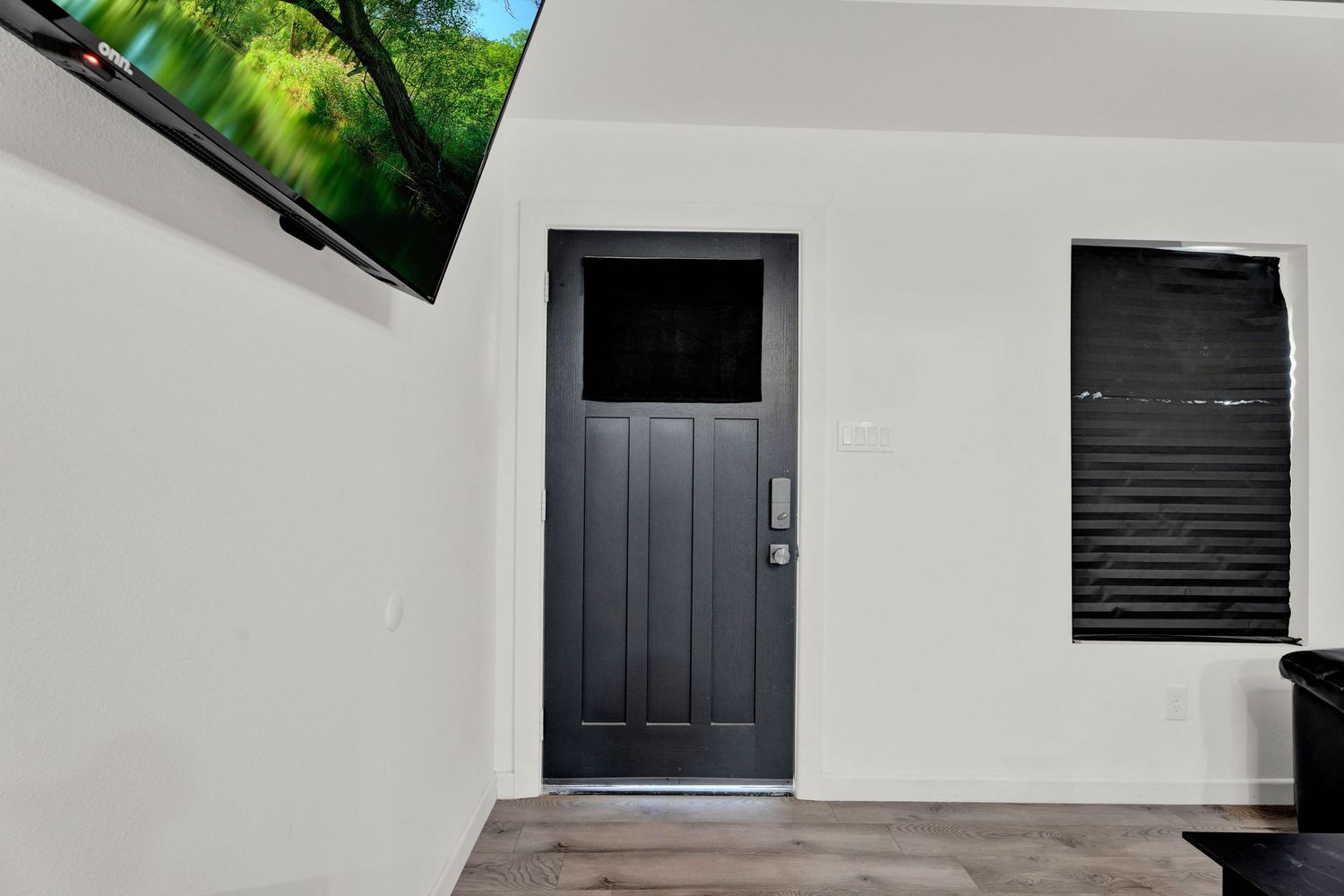 Modern dark gray front door with glass panel, smart lock, and black shuttered window on white exterior wall.