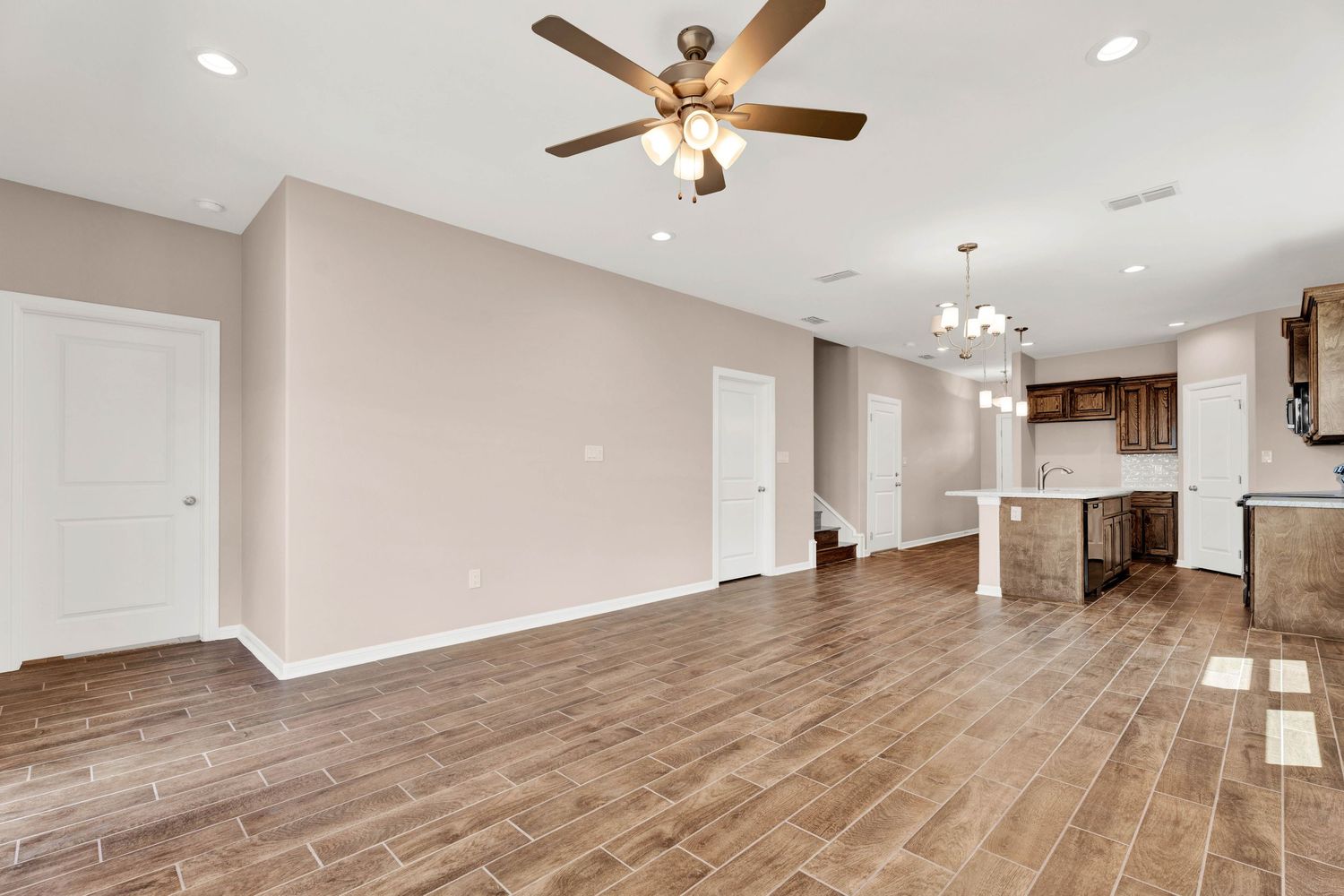 Open-concept living area with wood-look tile floors, ceiling fan, and view of kitchen with dark cabinetry and island.