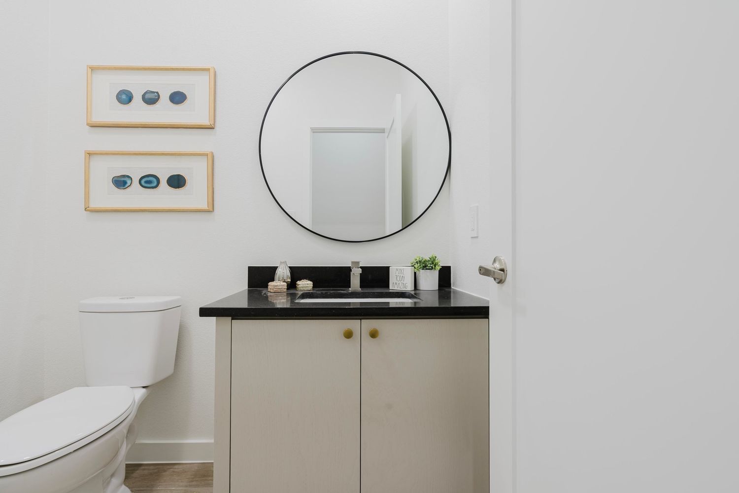 Modern bathroom vanity with round mirror, black countertop, and framed wall art.