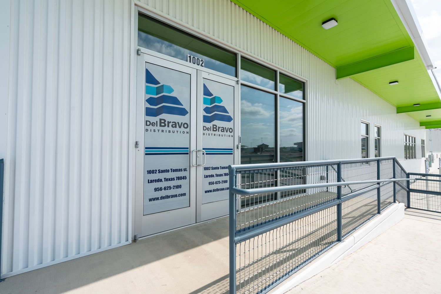 Modern white commercial building exterior with lime green accents and accessibility ramp featuring glass doors with business logos.