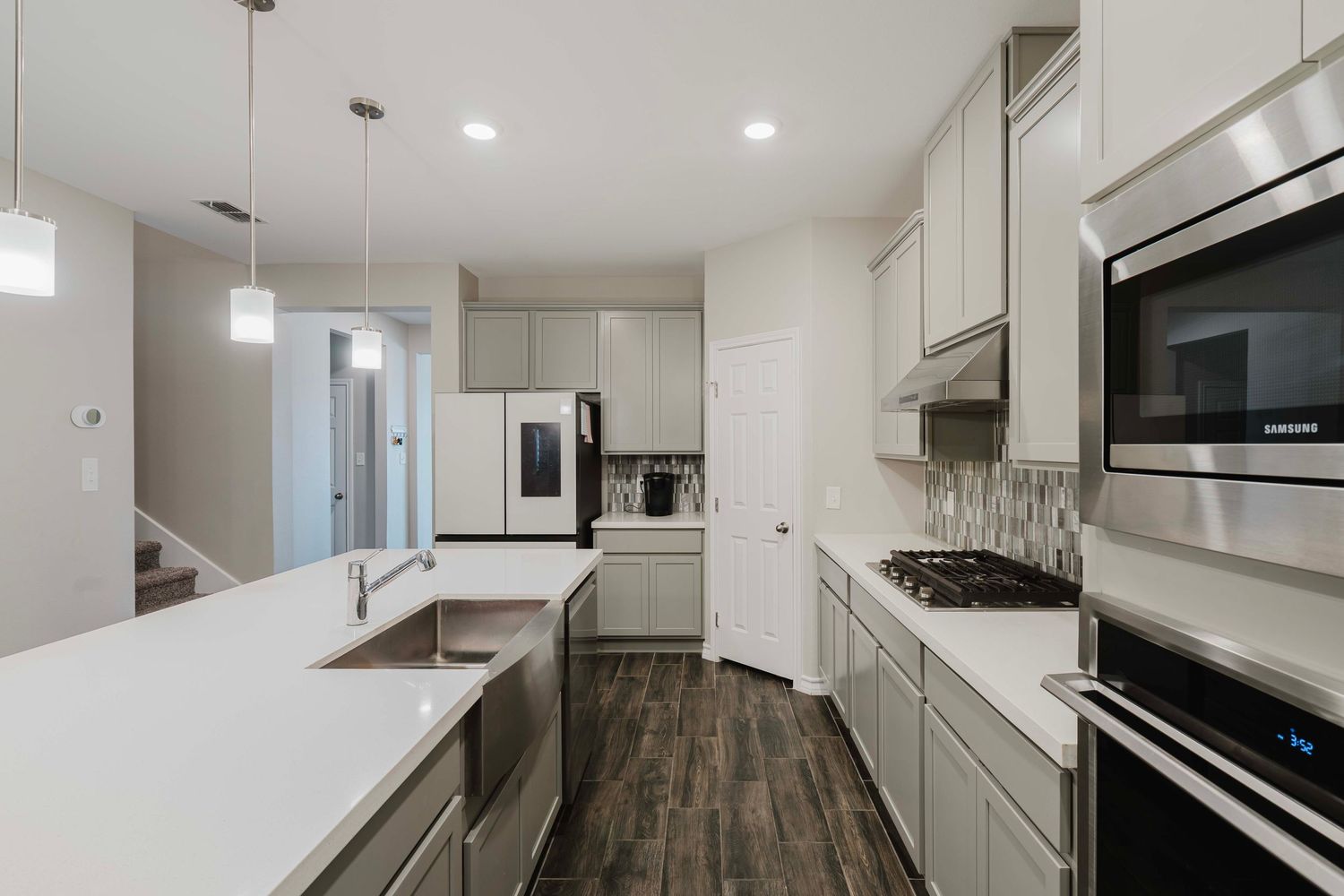 Contemporary white kitchen with quartz countertops, pendant lights, and stainless steel appliances.