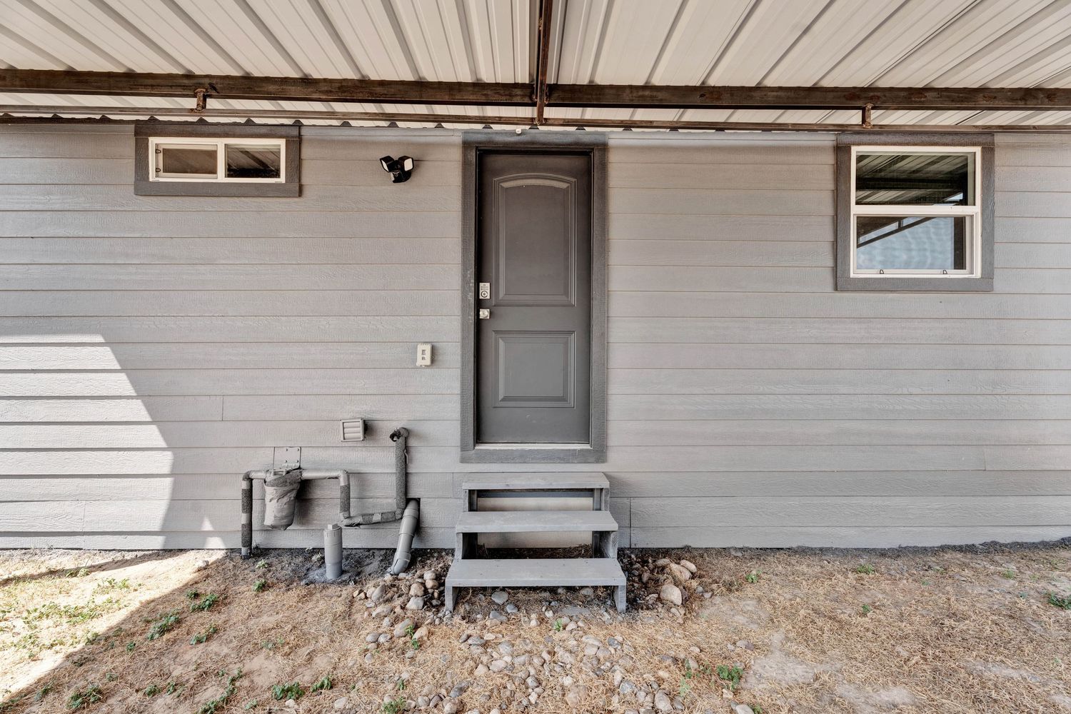 Gray siding home exterior featuring a gray front door with steps, security light, and covered porch overhang.
