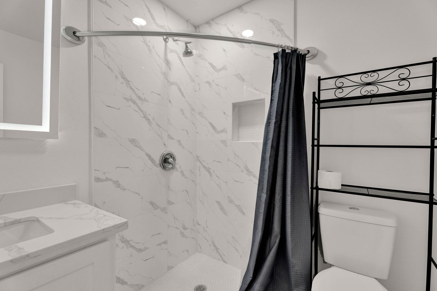 Modern bathroom with marble-style shower walls, black curtain rod, and white toilet and vanity.
