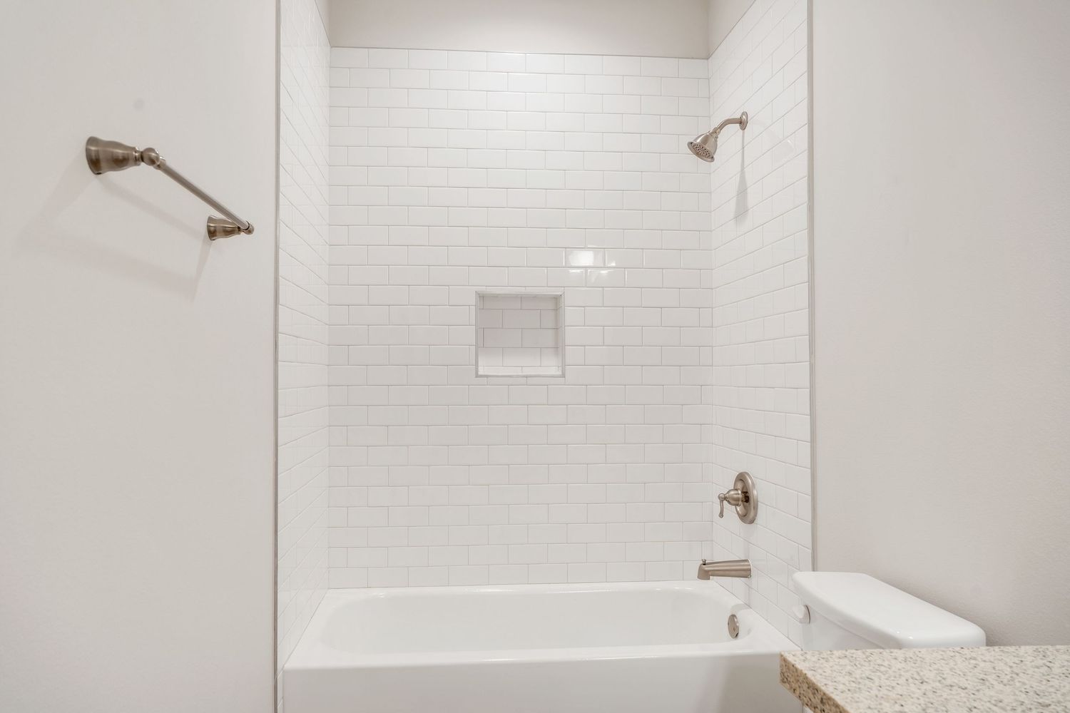 A clean white tiled bathroom interior with bronze fixtures and a glass shower enclosure.