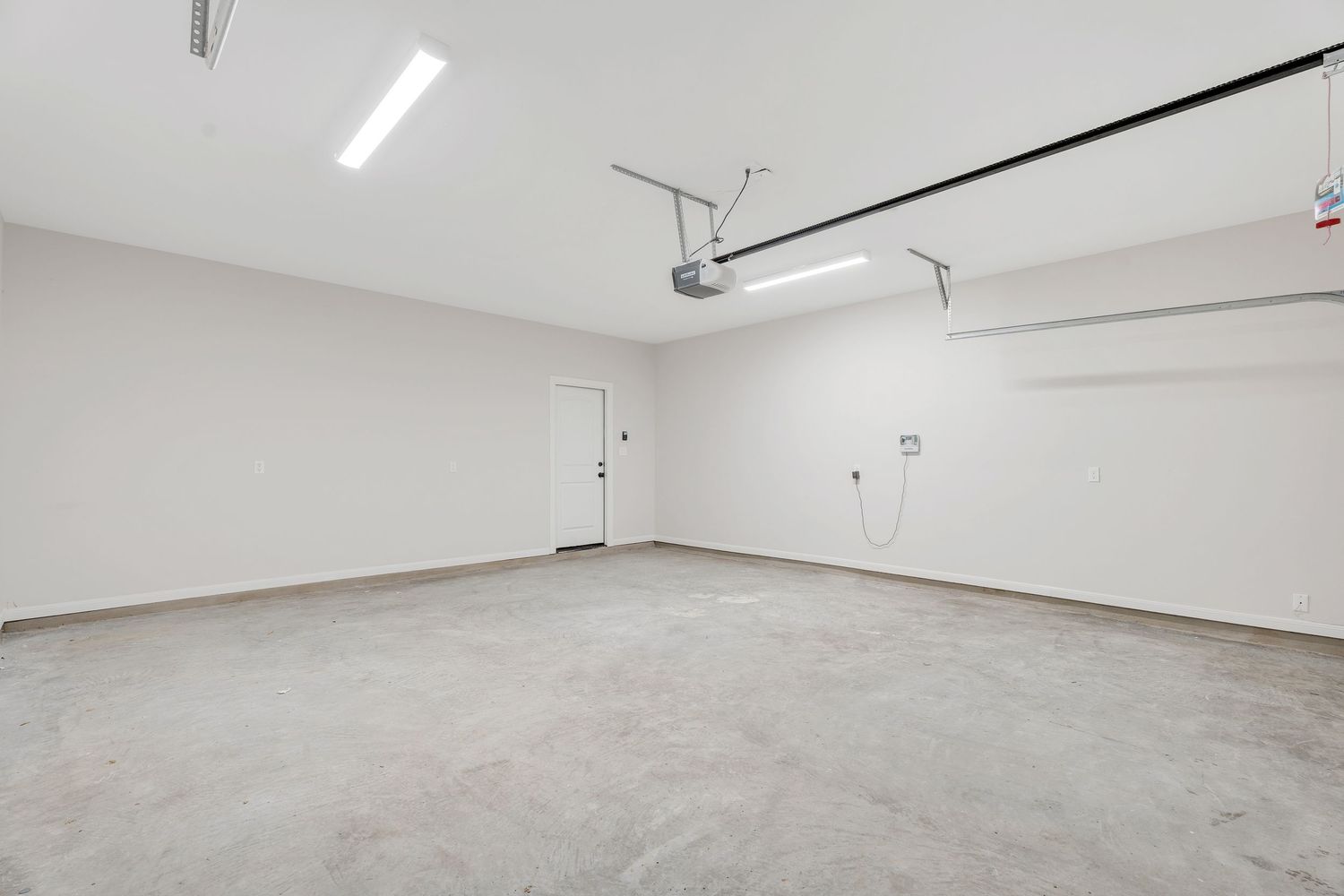 A bright, empty white room with fluorescent lighting on the ceiling and a smooth concrete floor.