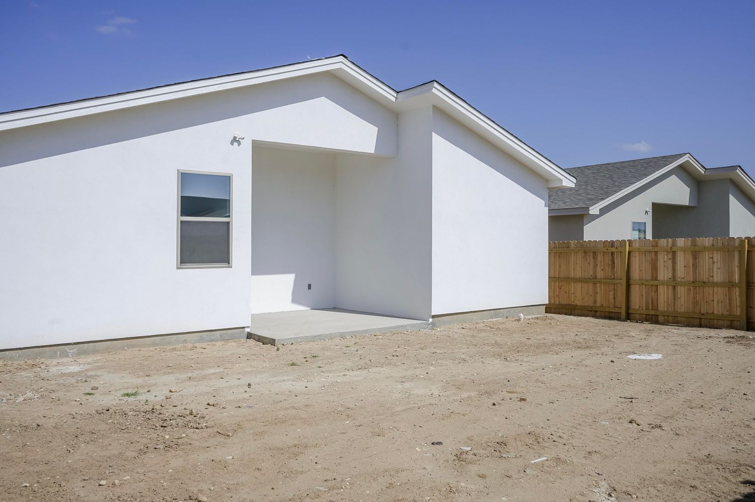 Side view of white modern house with pitched roof and wooden fence.
