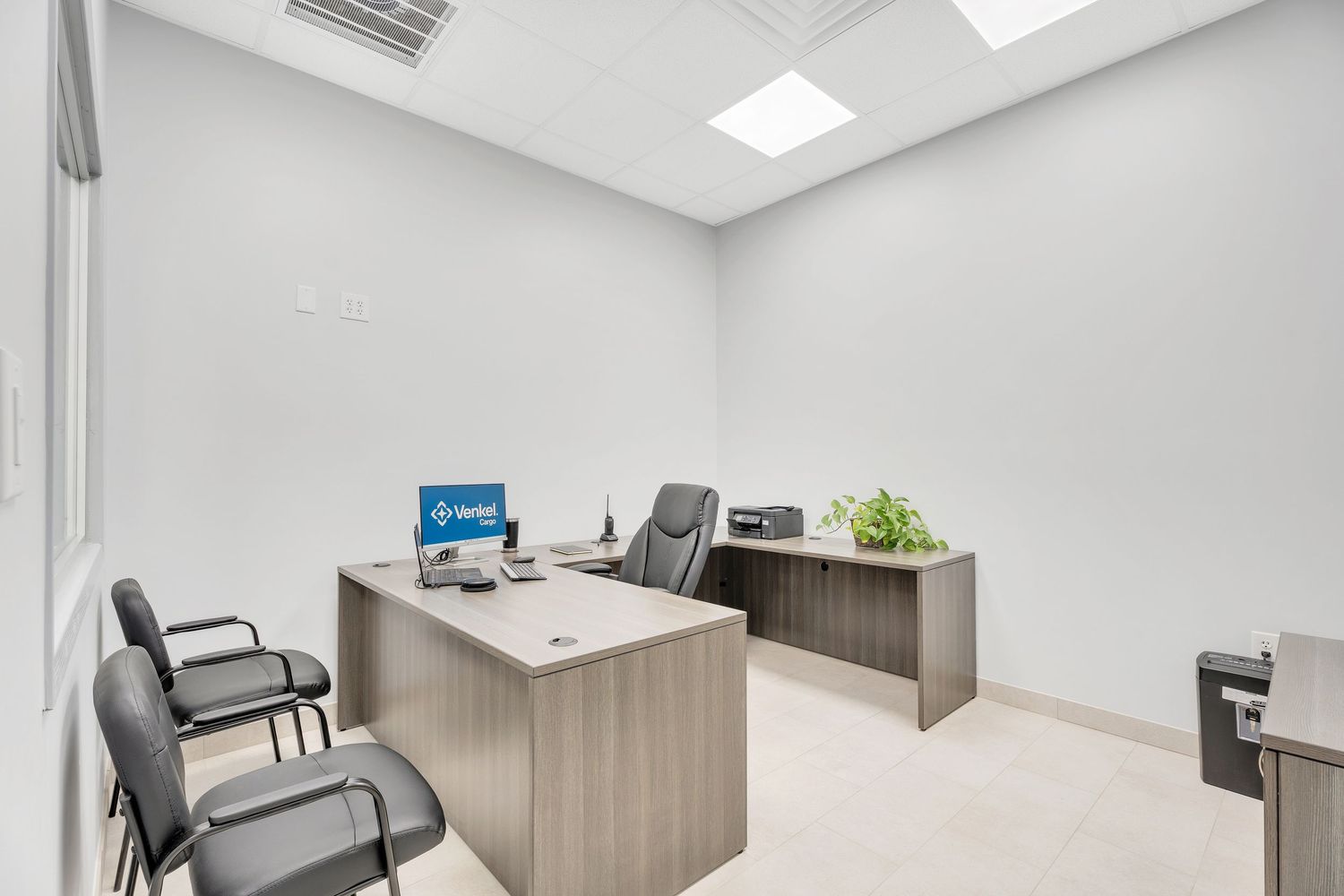 Modern office interior with light wood desk, gray chairs, and white walls illuminated by recessed lighting.