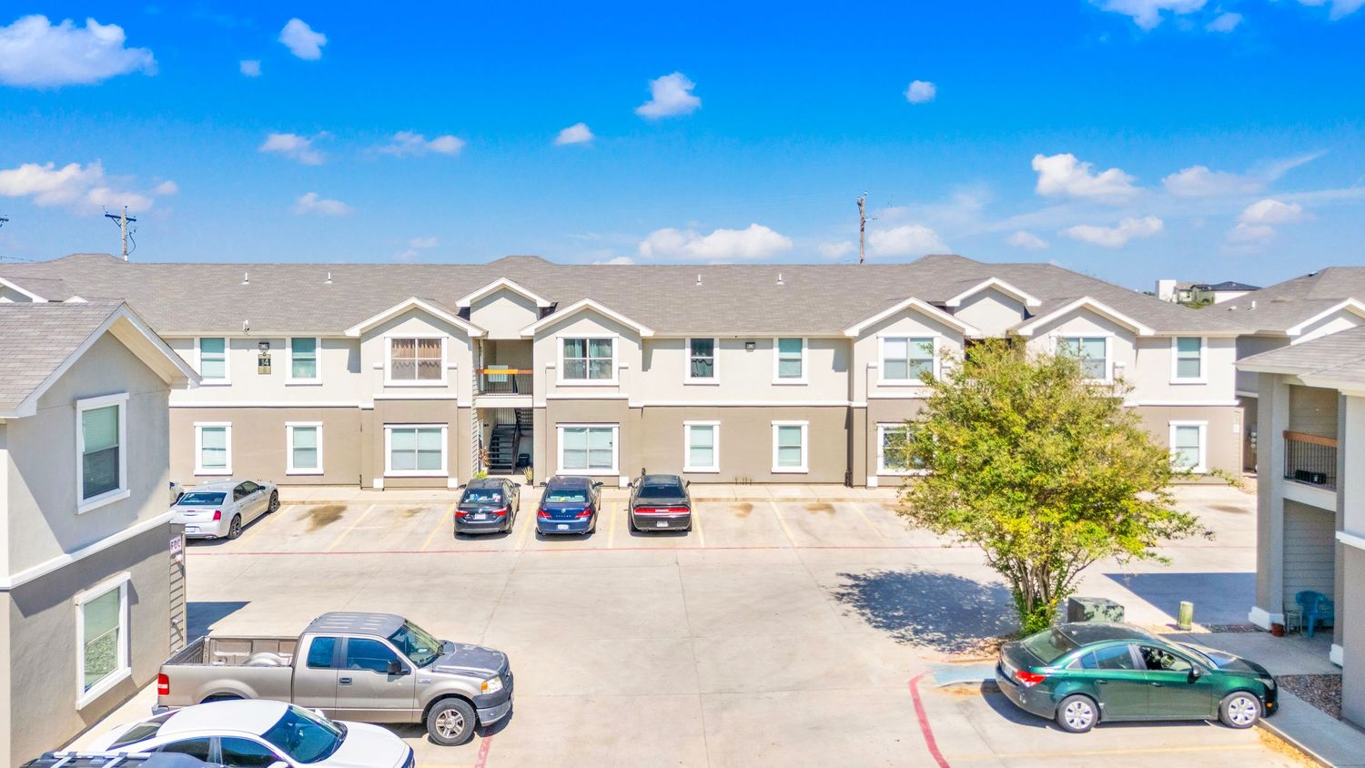 Wide angle view of modern townhouse complex with parked cars and landscaping on a sunny day.