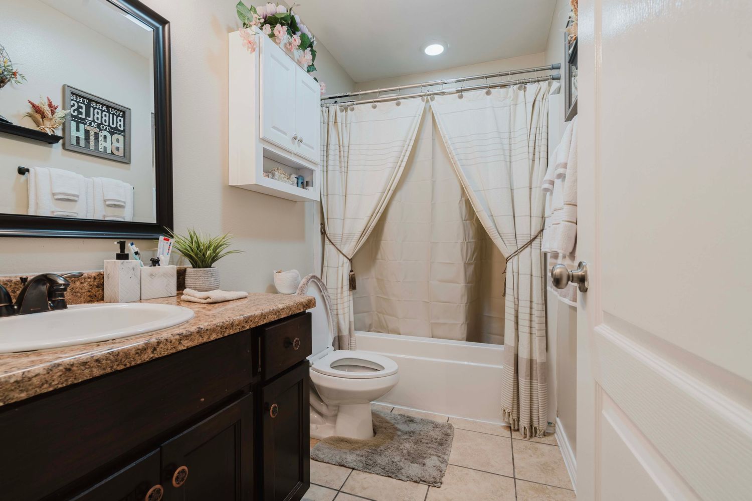 Modern bathroom interior with dark wood vanity, granite countertop, beige curtains and decorative wall accents.