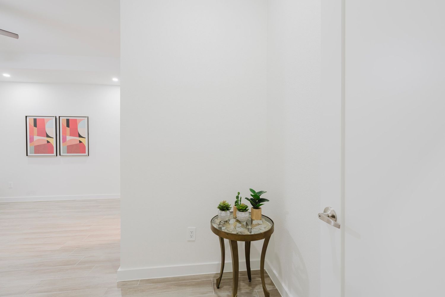 White hallway with geometric art prints and small round accent table.