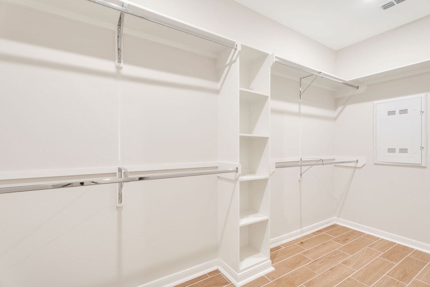 Empty white-walled room with hardwood flooring, exposed ceiling beams, and recessed lighting in a modern industrial style.