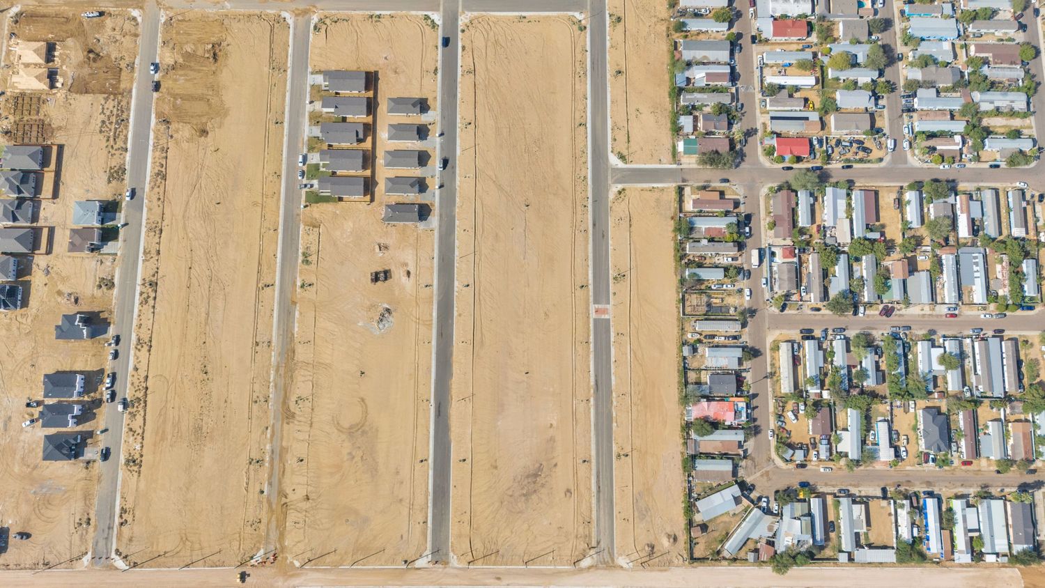 Aerial view of a mobile home park with rows of trailers adjacent to undeveloped desert land.