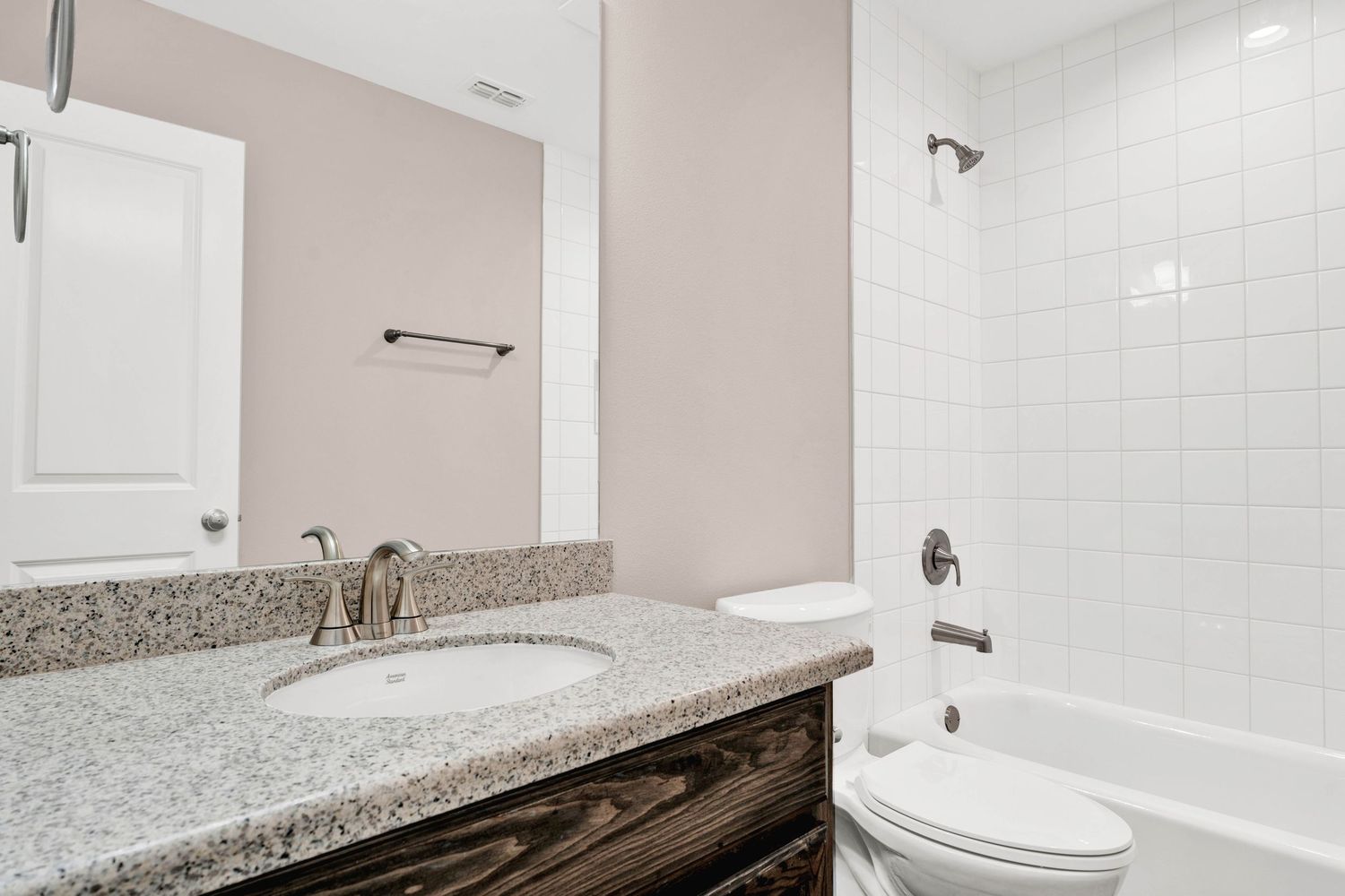 Modern bathroom with granite countertop vanity, white subway tile tub surround, and toilet in neutral tones.