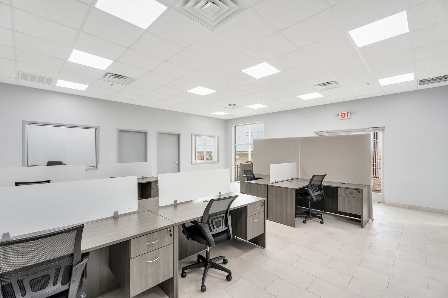 Modern office workspace with white desks, ergonomic chairs, and bright fluorescent lighting in a clean corporate setting.