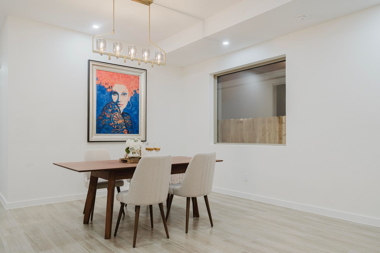 Minimalist dining area with blue artwork, modern pendant light fixture and white upholstered chairs.